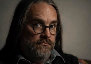 Colour Headshot photo of a man with long hair and beard