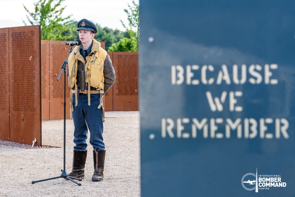 Young man in Bomber Command aircrew uniform standing beside a plaque.